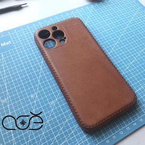 Brown leather phone case on a blue cutting mat with a logo in the corner.