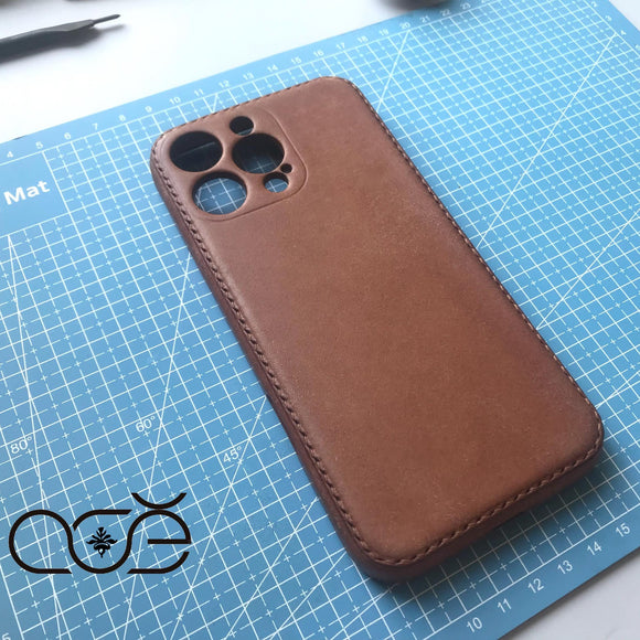Brown leather phone case on a blue cutting mat with a logo in the corner.